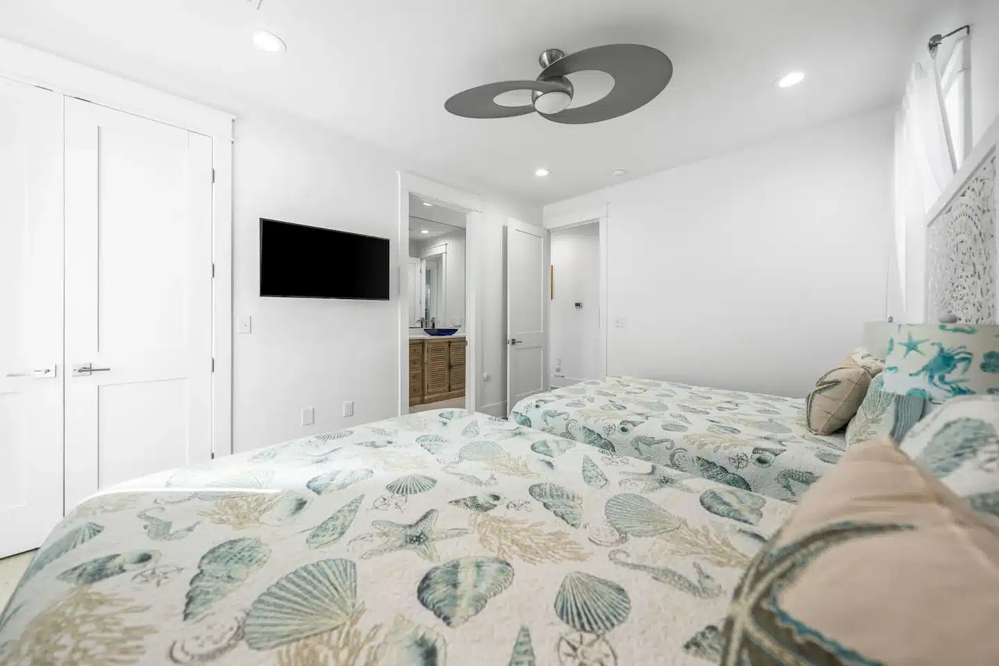 Bright master bedroom with two beds in cream and turquoise shell bedding, flat-screen TV and ceiling fan at Ocean Breeze, a