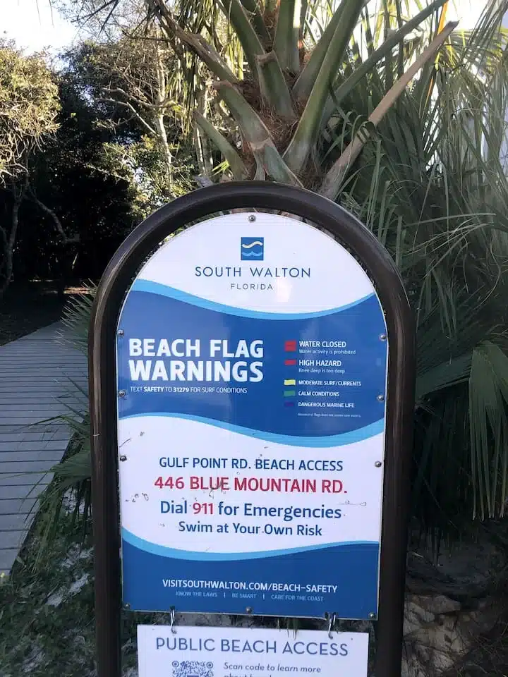 South Walton beach warning sign under palm trees near Ocean Breeze property in Blue Mountain Beach